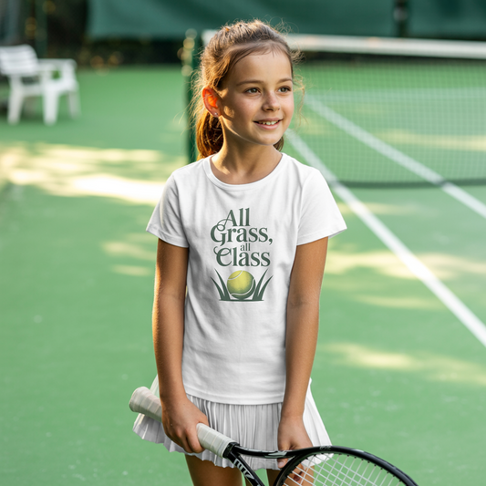 Young girl standing on a grass tennis court and wearing a white girls’ tennis T-shirt with green text “All Grass, All Class” and tennis ball in grass graphic.