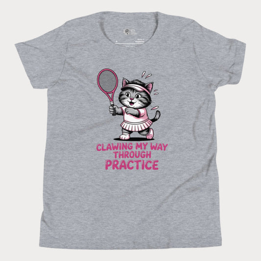 A grey girls’ tennis t-shirt featuring a determined gray kitten in a pink tennis outfit holding a pink tennis racket. The kitten is sweating and focused, with the phrase “Clawing My Way Through Practice” in bold pink lettering underneath.