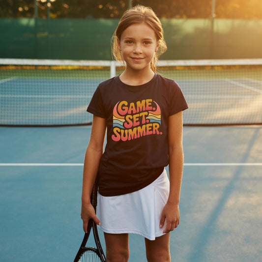 Tween girl standing on a tennis court and wearing a Game Set Summer tennis t-shirt with retro sunset design for players and fans.