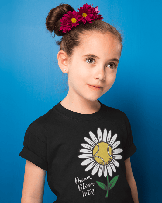 A young girl wearing a cute black girls' tennis t-shirt featuring a daisy with a tennis ball center and the motivational slogan "Dream, Bloom, WIN!"