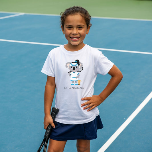 Young girl standing on a tennis court, holding a tennis racket and wearing a Little Aussie Ace kids tennis t-shirt with koala player illustration for toddlers and youth.