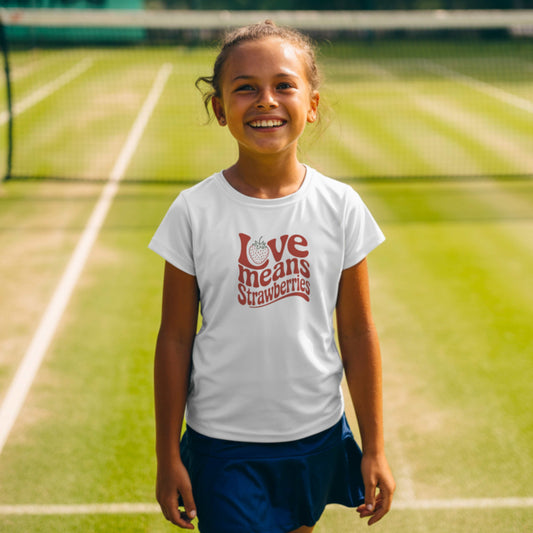 Young girl standing on a grass tennis court and wearing a white girls’ tennis T-shirt with retro red “Love Means Strawberries” slogan and cute illustrated strawberry.