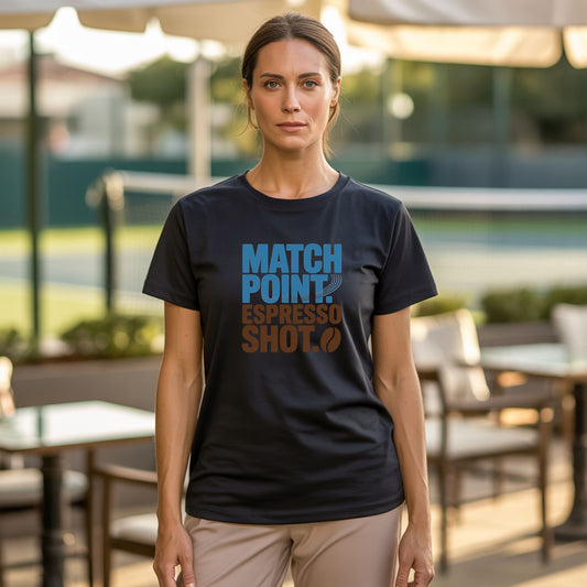 A women standing in a coffee shop next to a tennis court, wearing black tennis t-shirt with Match Point Espresso Shot typography design for fans for tennis and coffee.
