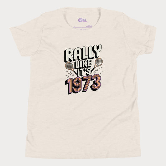 Beige girls tennis t-shirt with retro slogan ‘Rally Like It’s 1973’ and crossed tennis rackets