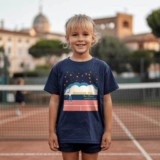 Girls standing on a clay tennis court and wearing a navy girls' tennis T-shirt featuring a motivational design of a young girl serving on a tennis court under a starry sky, with the phrase "Reaching for the Stars, One Serve at a Time." Perfect for young tennis players who dream big.