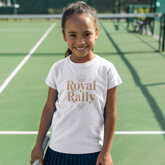 Young girl standing on a green tennis court and wearing a white girls’ tennis t-shirt with gold “Royal Rally” crown and rackets design.