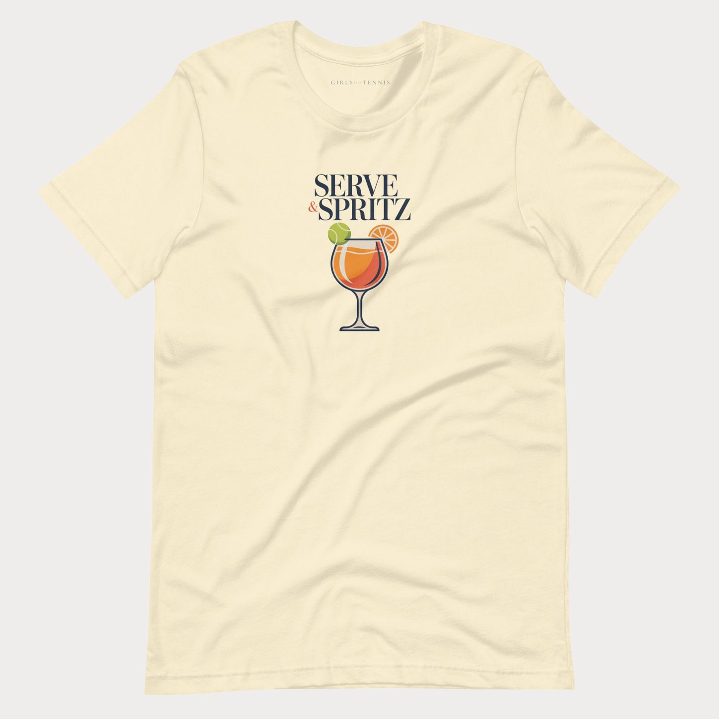 A cream-colored short-sleeve tennis lifestyle t-shirt with a graphic on the chest that reads 'SERVE & SPRITZ' above an illustration of a cocktail with a tennis ball and orange slice.