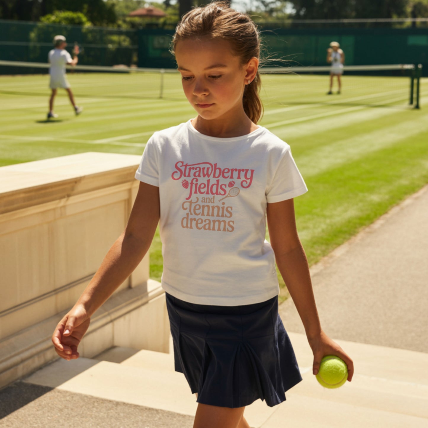 Young girl wearing a white girls tennis t-shirt with retro text that reads ‘Strawberry fields and tennis dreams’ with tennis and strawberry icons