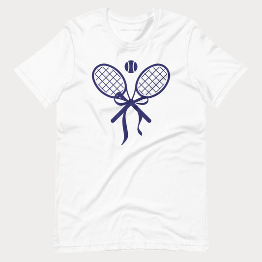 A white short-sleeve crewneck tennis t-shirt featuring a navy blue graphic of two tennis rackets tied in a bow with a tennis ball above them, displayed on a light gray background.