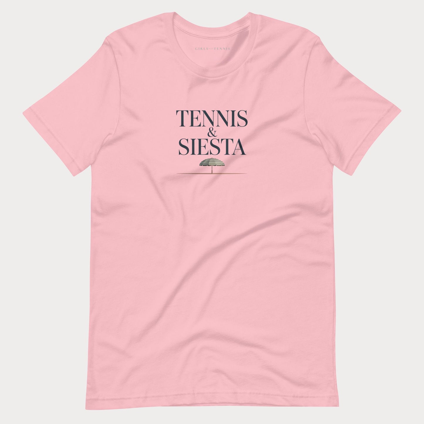 A light pink short-sleeve crewneck women's lifestyle t-shirt with 'TENNIS & SIESTA' printed in dark navy text on the chest, accompanied by a small green umbrella graphic, displayed on a light gray background.