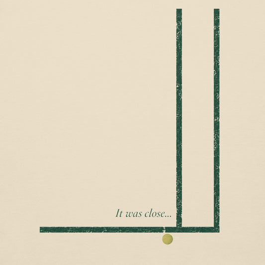 Close-up of the worn forest green court-corner lines, a tennis ball just past the line and the script caption It was close... on a bone It Was Close... crewneck sweatshirt