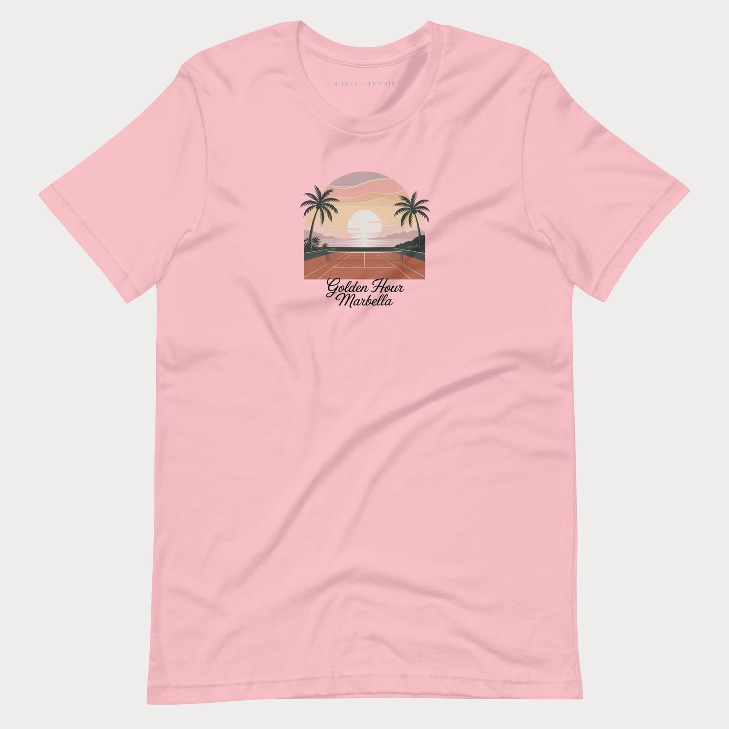 A light pink short-sleeve crewneck t-shirt featuring a retro-style graphic of a sunset over a tropical beach with palm trees and the text 'Golden Hour Mediterranean' printed on the chest, displayed against a light gray background.
