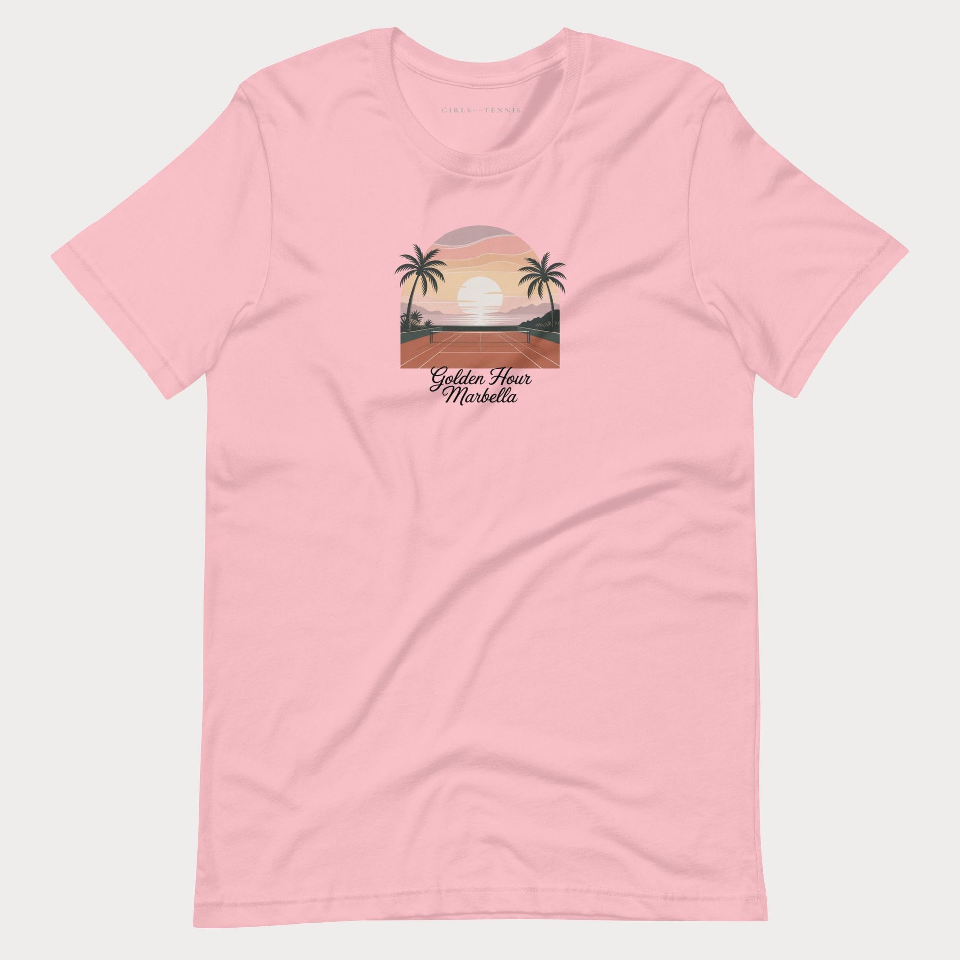 A light pink short-sleeve crewneck t-shirt featuring a retro-style graphic of a sunset over a tropical beach with palm trees and the text 'Golden Hour Mediterranean' printed on the chest, displayed against a light gray background.