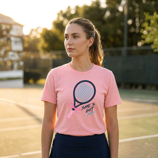 Woman wearing a pink t-shirt with a tennis racket graphic on a tennis court