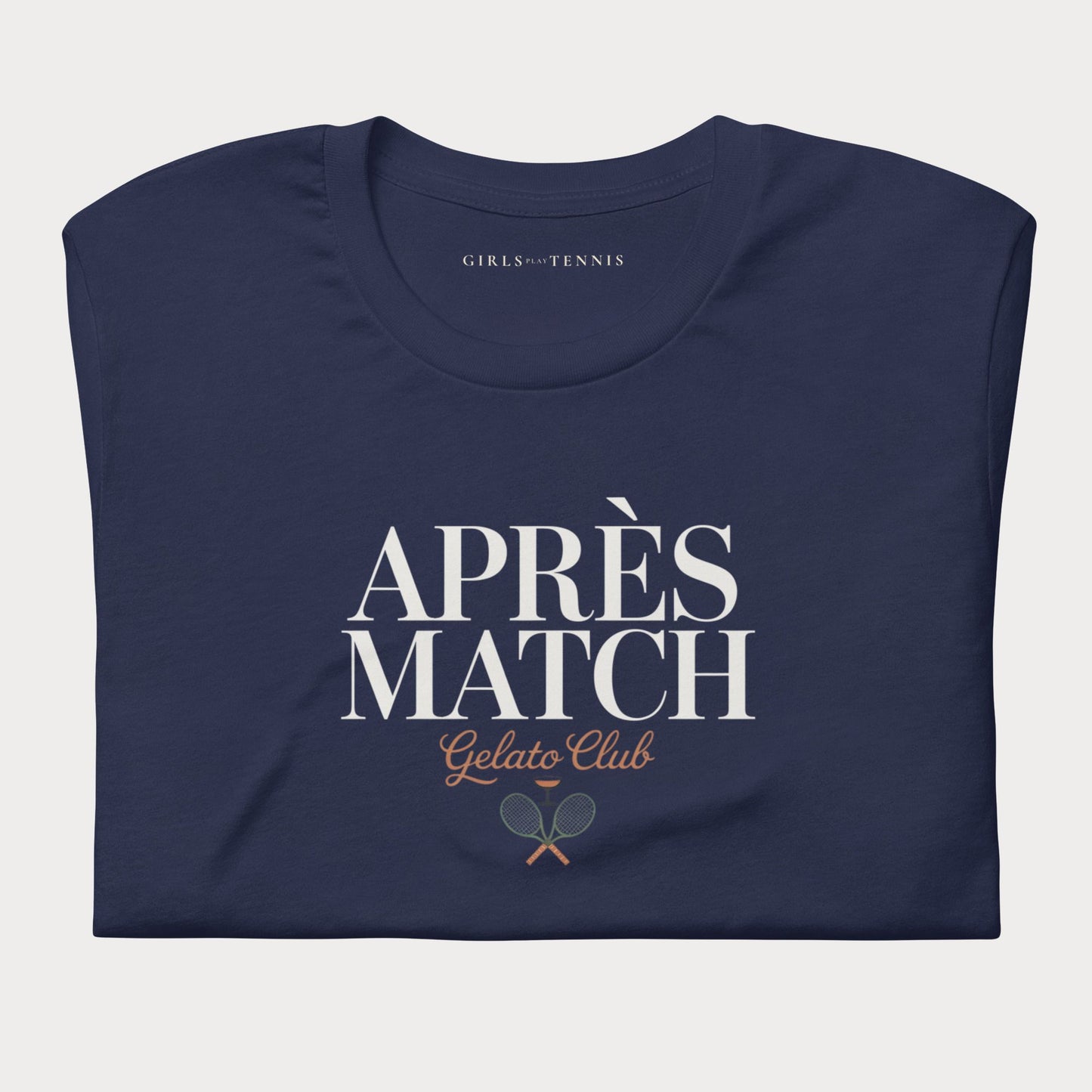 A navy blue folded t-shirt with a graphic print reading 'APRÈS MATCH Gelato Club' and a small tennis racket graphic, on a light gray background.