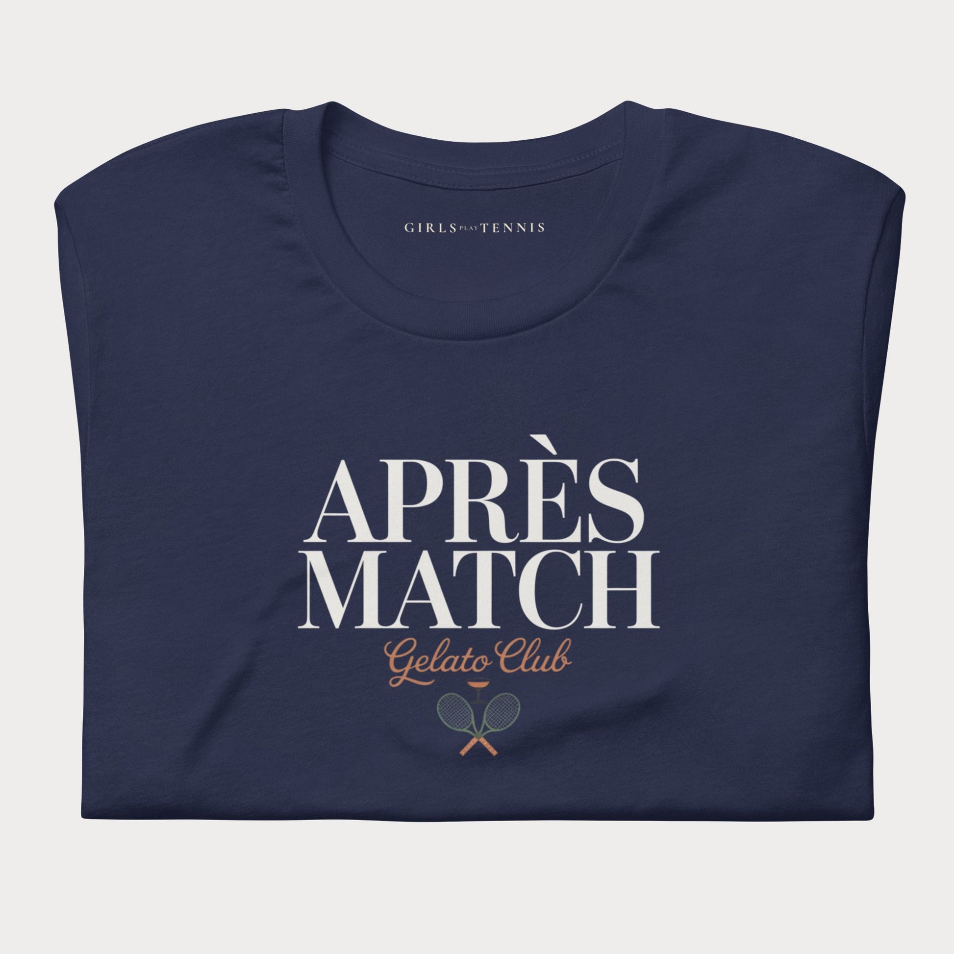 A navy blue folded t-shirt with a graphic print reading 'APRÈS MATCH Gelato Club' and a small tennis racket graphic, on a light gray background.