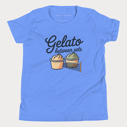 A light blue short-sleeve t-shirt with a graphic print that reads 'Gelato between sets' above two illustrated gelato cups and a tennis net. The inner collar shows the brand name 'GIRLS PLAY TENNIS'.