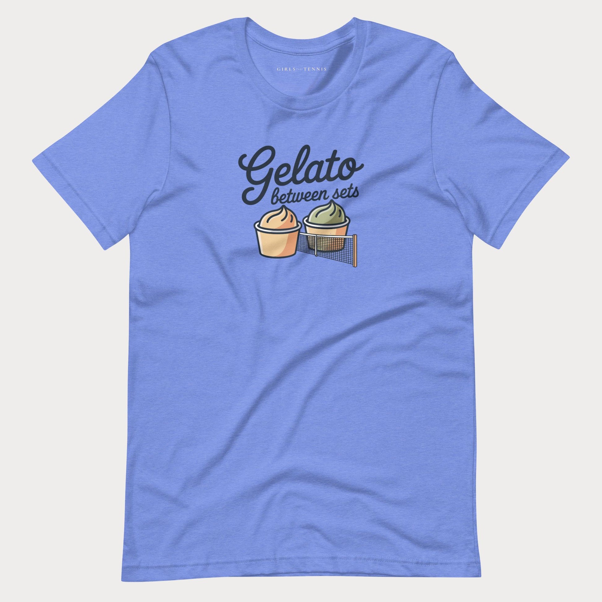 A heather blue short-sleeve women's tennis t-shirt with a graphic on the chest that reads 'Gelato between sets' above two illustrated gelato cups, shown on a light gray background.