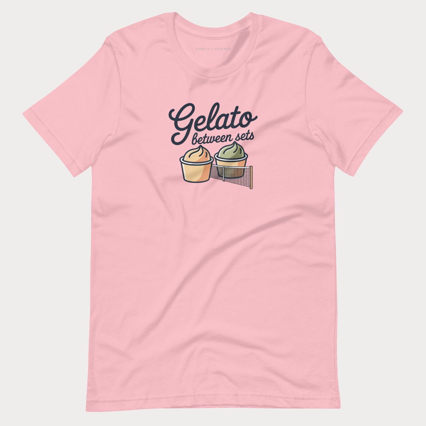 A light pink short-sleeve women's tennis t-shirt with a graphic on the chest that reads 'Gelato between sets' above two illustrated gelato cones, shown on a light gray background.