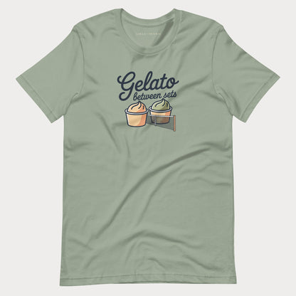 A sage green short-sleeve women's tennis t-shirt with a graphic on the chest that reads 'Gelato between sets' above two illustrated dessert cups on a tennis net.