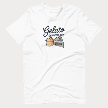 A white short-sleeve crewneck women's tennis t-shirt featuring a graphic print of two gelato cups separated by a net, with the text 'Gelato between sets' written above them.