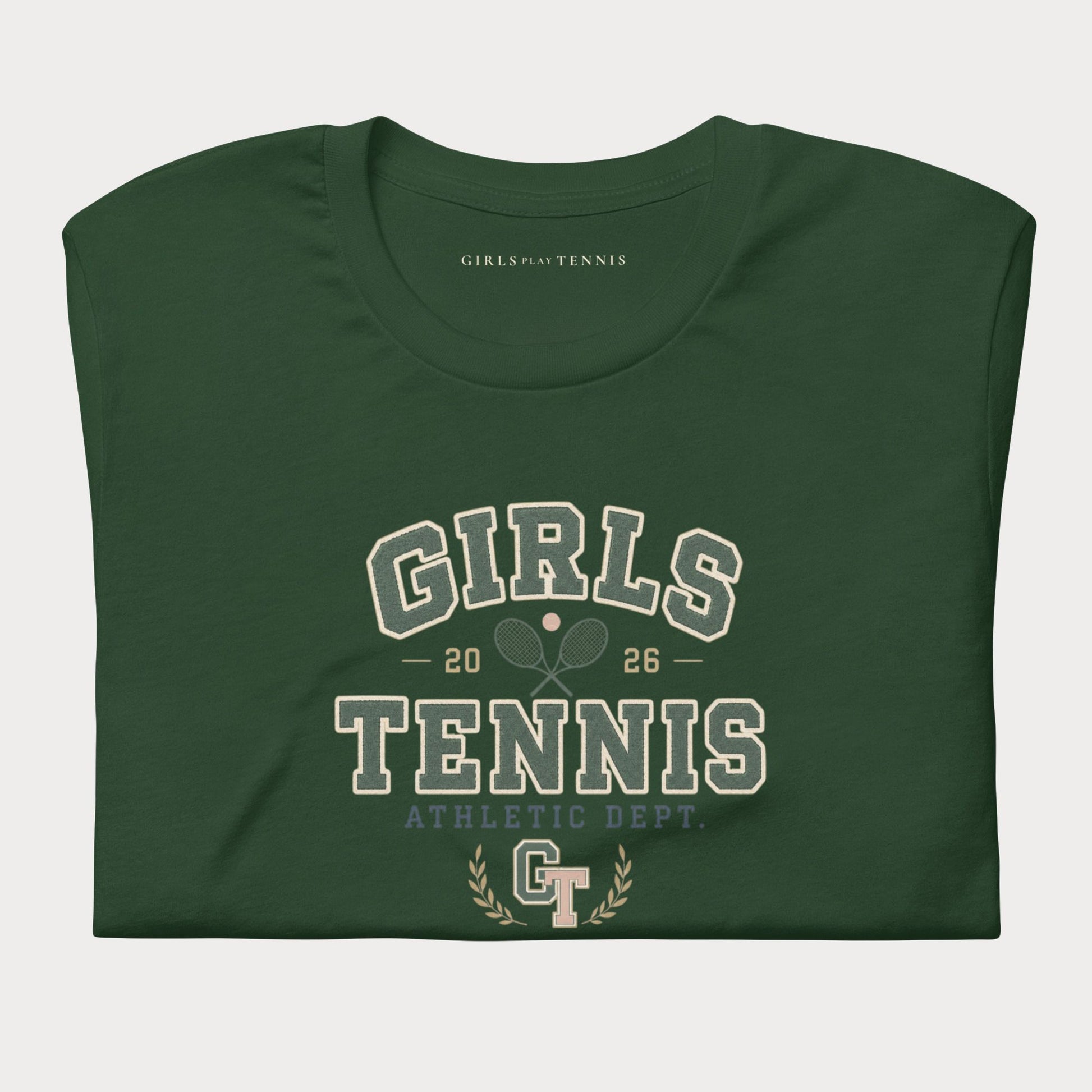 A dark green folded t-shirt with a vintage-style collegiate graphic reading 'GIRLS TENNIS' and 'ATHLETIC DEPT.' in cream and light blue-gray lettering, on a light gray background.