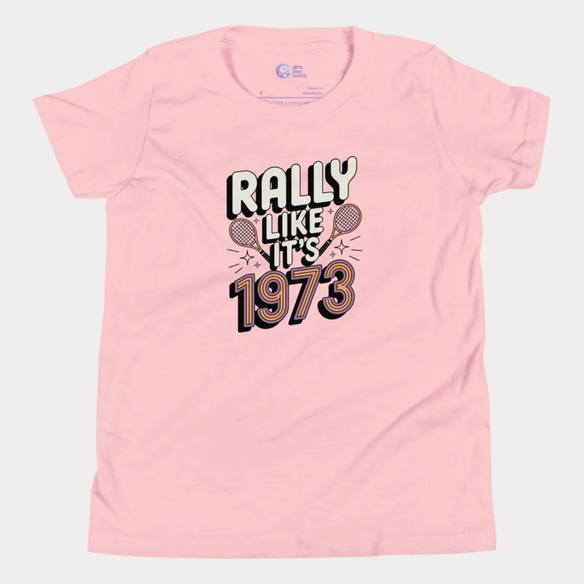 Pink girls tennis t-shirt with retro slogan ‘Rally Like It’s 1973’ and crossed tennis rackets.