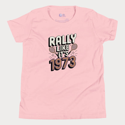 Pink girls tennis t-shirt with retro slogan ‘Rally Like It’s 1973’ and crossed tennis rackets.
