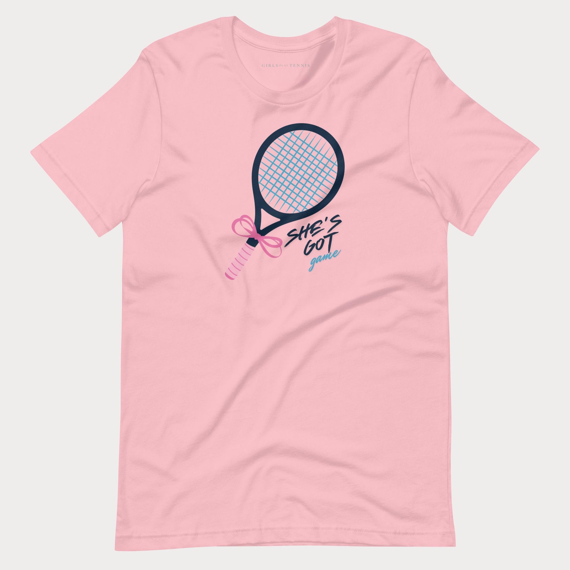 A light pink short-sleeve t-shirt with a graphic of a tennis racket and the text 'SHE'S GOT game' in black, pink, and blue, displayed on a light gray background.