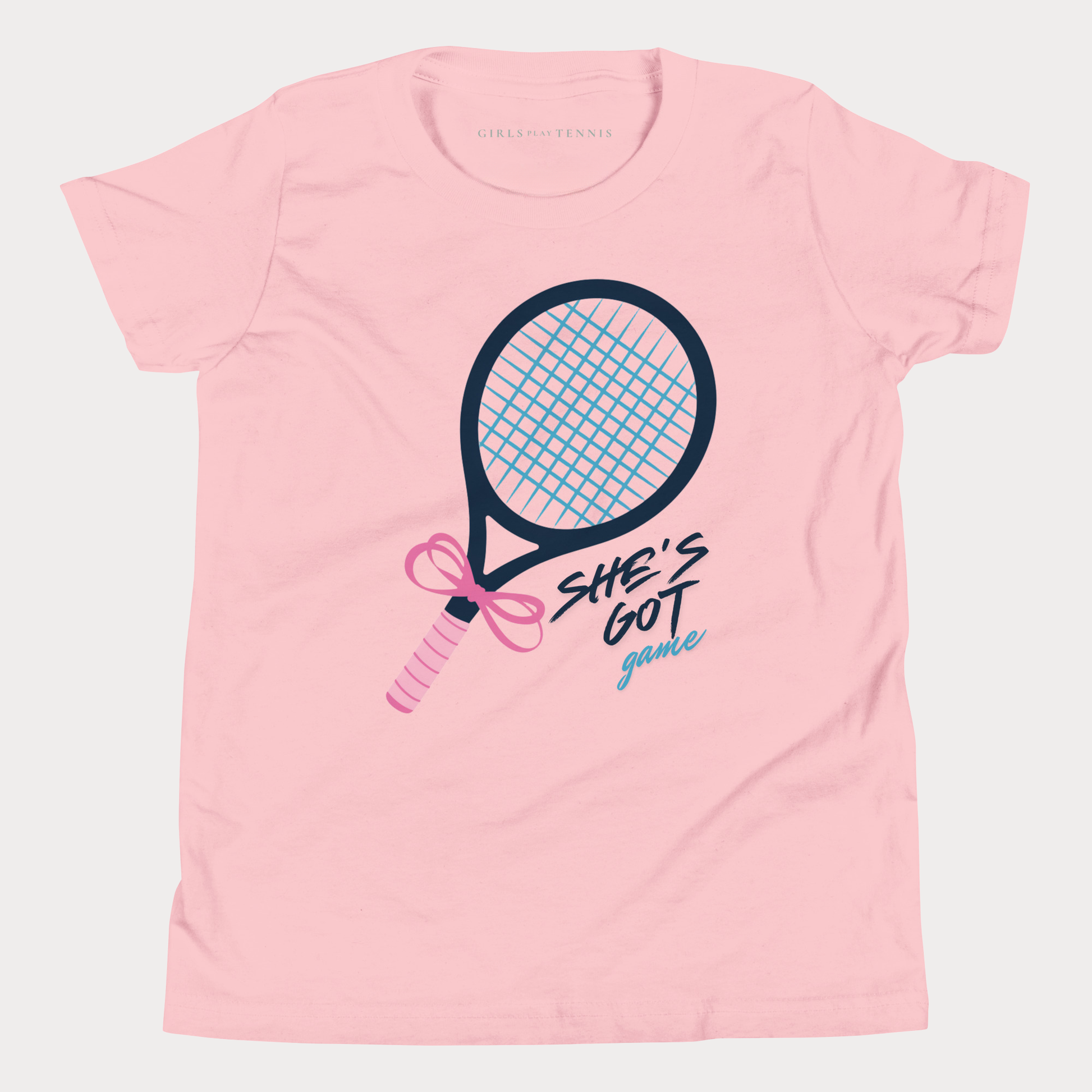 A light pink short-sleeve t-shirt with a graphic of a tennis racket and the text 'SHE'S GOT game' in black and light blue, on a light gray background.