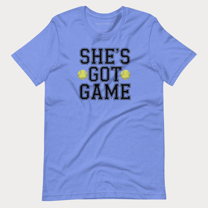 A heather blue short-sleeve women's tennis t-shirt with a graphic on the front that reads 'SHE'S GOT GAME' in black varsity-style letters, accented by two yellow tennis balls, shown on a light gray background.