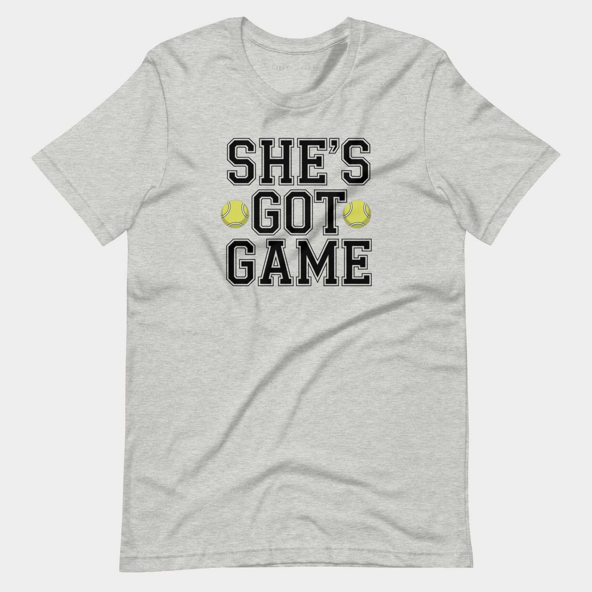 A light heather gray short-sleeve women's tennis t-shirt with a graphic print on the front that reads 'SHE'S GOT GAME' in black varsity-style letters, accented by two yellow tennis balls.