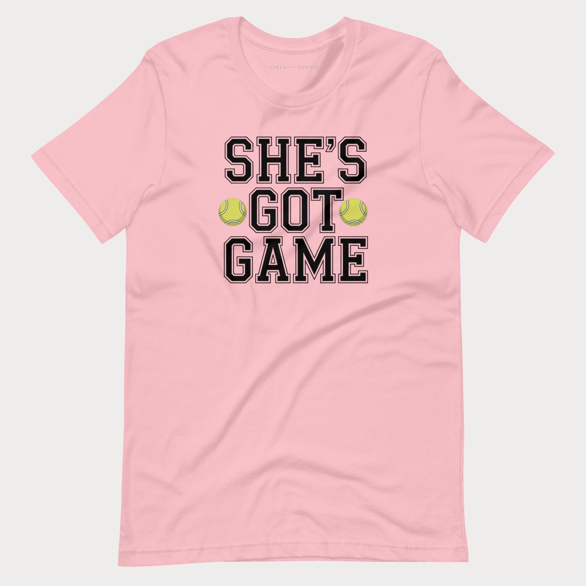 A light pink short-sleeve crewneck women's tennis t-shirt featuring the text 'SHE'S GOT GAME' in black varsity-style lettering with a thin white outline, accented by two yellow-green tennis balls between the words 'GOT' and 'GAME'.