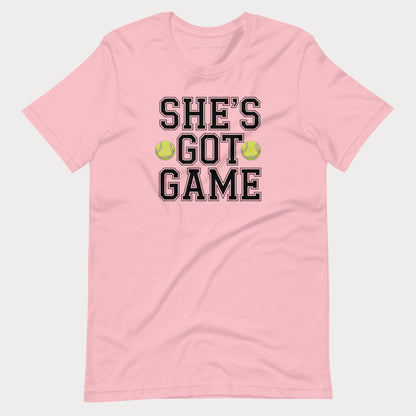 A light pink short-sleeve crewneck women's tennis t-shirt featuring the text 'SHE'S GOT GAME' in black varsity-style lettering with a thin white outline, accented by two yellow-green tennis balls between the words 'GOT' and 'GAME'.