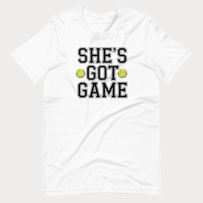 A white short-sleeve crewneck women's tennis t-shirt featuring the text 'SHE'S GOT GAME' in a black varsity-style font with a white outline, accented by two yellow-green tennis balls between the words 'GOT' and 'GAME'.