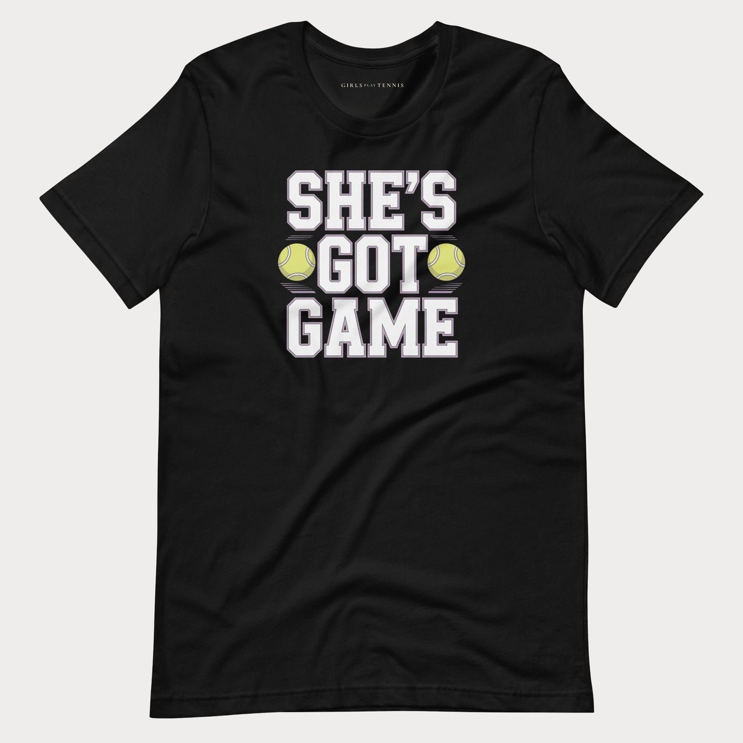 A black short-sleeve women's tennis t-shirt with a graphic print that reads 'SHE'S GOT GAME' in white block letters, accented by two yellow tennis balls, shown on a light gray background.