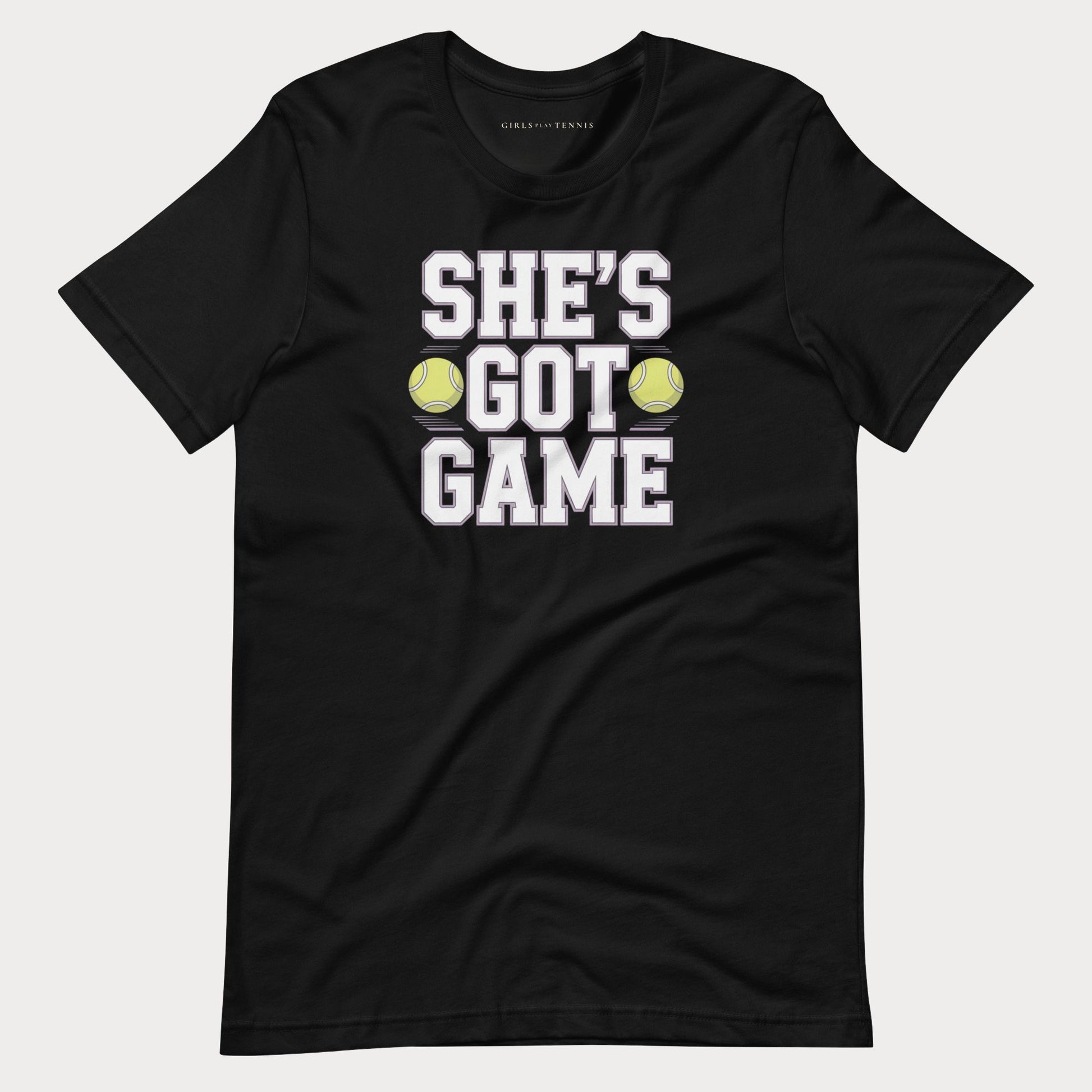 A black short-sleeve women's tennis t-shirt with a graphic print that reads 'SHE'S GOT GAME' in white block letters, accented by two yellow tennis balls, shown on a light gray background.