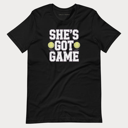 A black short-sleeve women's tennis t-shirt with a graphic print that reads 'SHE'S GOT GAME' in white block letters, accented by two yellow tennis balls, shown on a light gray background.