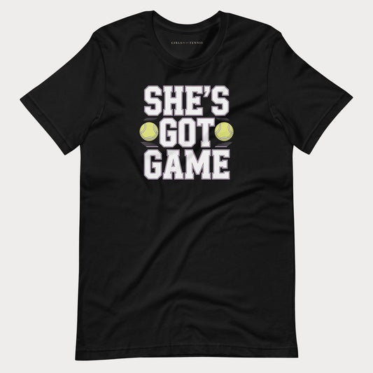 A black short-sleeve women's tennis t-shirt with a graphic print that reads 'SHE'S GOT GAME' in white block letters, accented by two yellow tennis balls, shown on a light gray background.