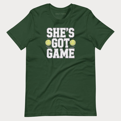 A dark green short-sleeve women's tennis t-shirt with a graphic print on the front that reads 'SHE'S GOT GAME' in white block letters, with two yellow tennis balls replacing the 'O' in 'GOT'.