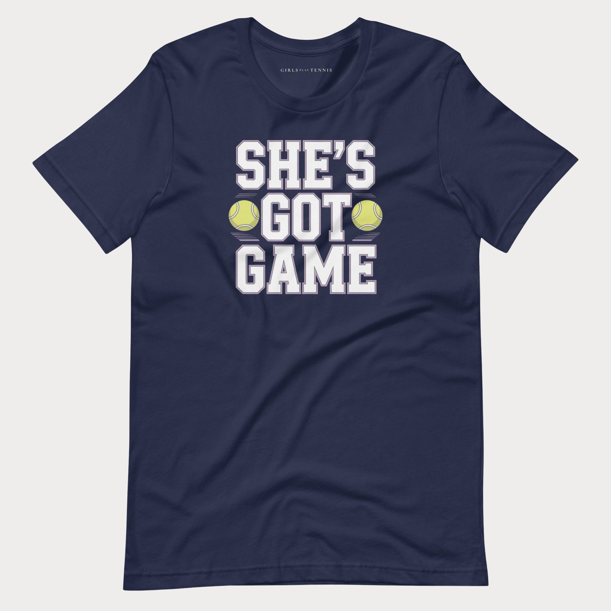 A navy blue short-sleeve women's tennis t-shirt with a graphic print that reads 'SHE'S GOT GAME' in white block letters, accented by two yellow tennis balls, shown on a light gray background.
