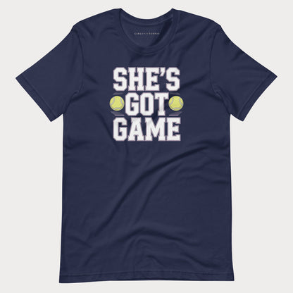 A navy blue short-sleeve women's tennis t-shirt with a graphic print that reads 'SHE'S GOT GAME' in white block letters, accented by two yellow tennis balls, shown on a light gray background.