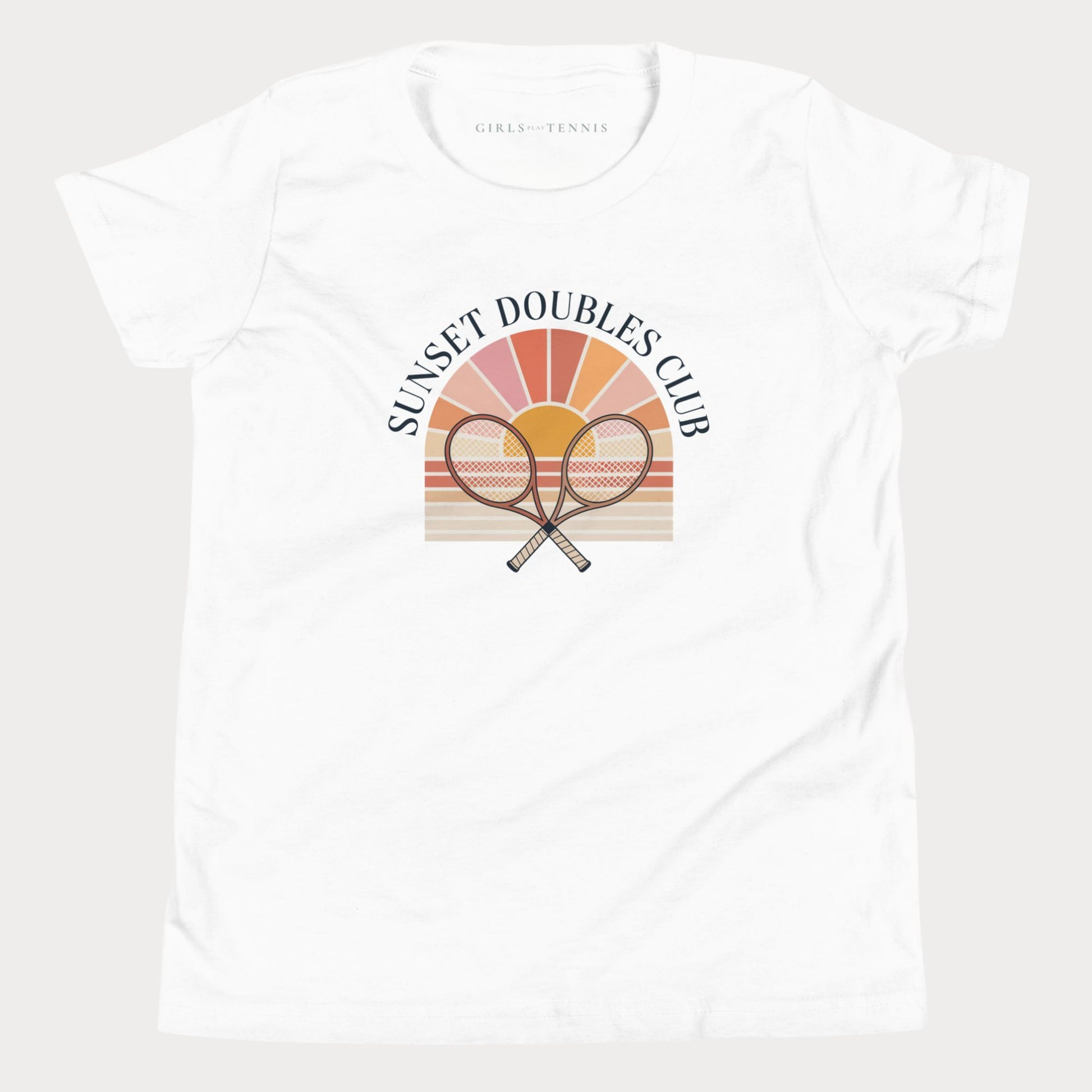 A white short-sleeve crewneck girls tennis t-shirt featuring a retro-style graphic on the front with two crossed tennis rackets in front of a sunset gradient and the text 'SUNSET DOUBLES CLUB'. The inner neck label reads 'GIRLS PLAY TENNIS'.
