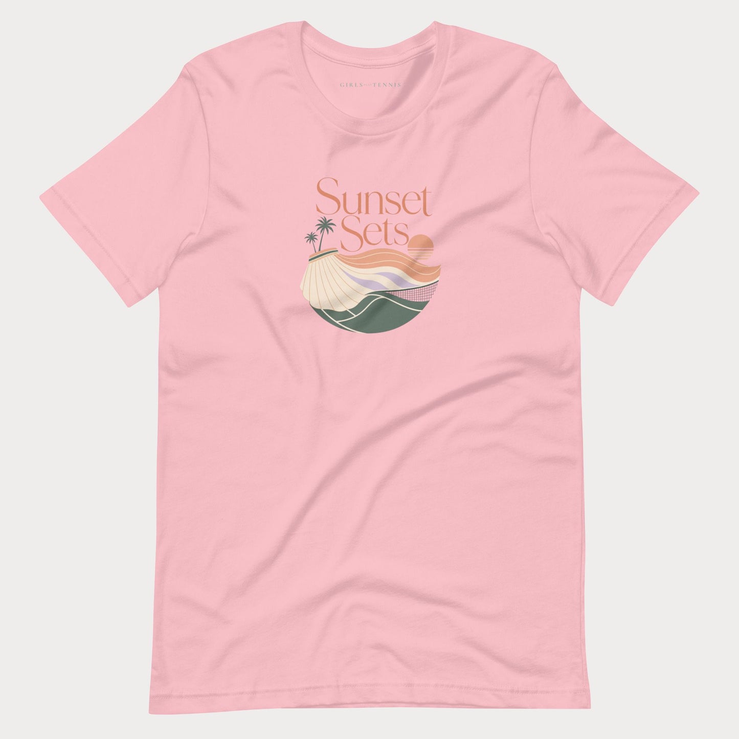 A light pink short-sleeve crewneck women's lifestyle tennis t-shirt featuring a retro-style graphic on the chest with the text 'Sunset Sets' above a stylized beach scene with palm trees, a sun, and waves.
