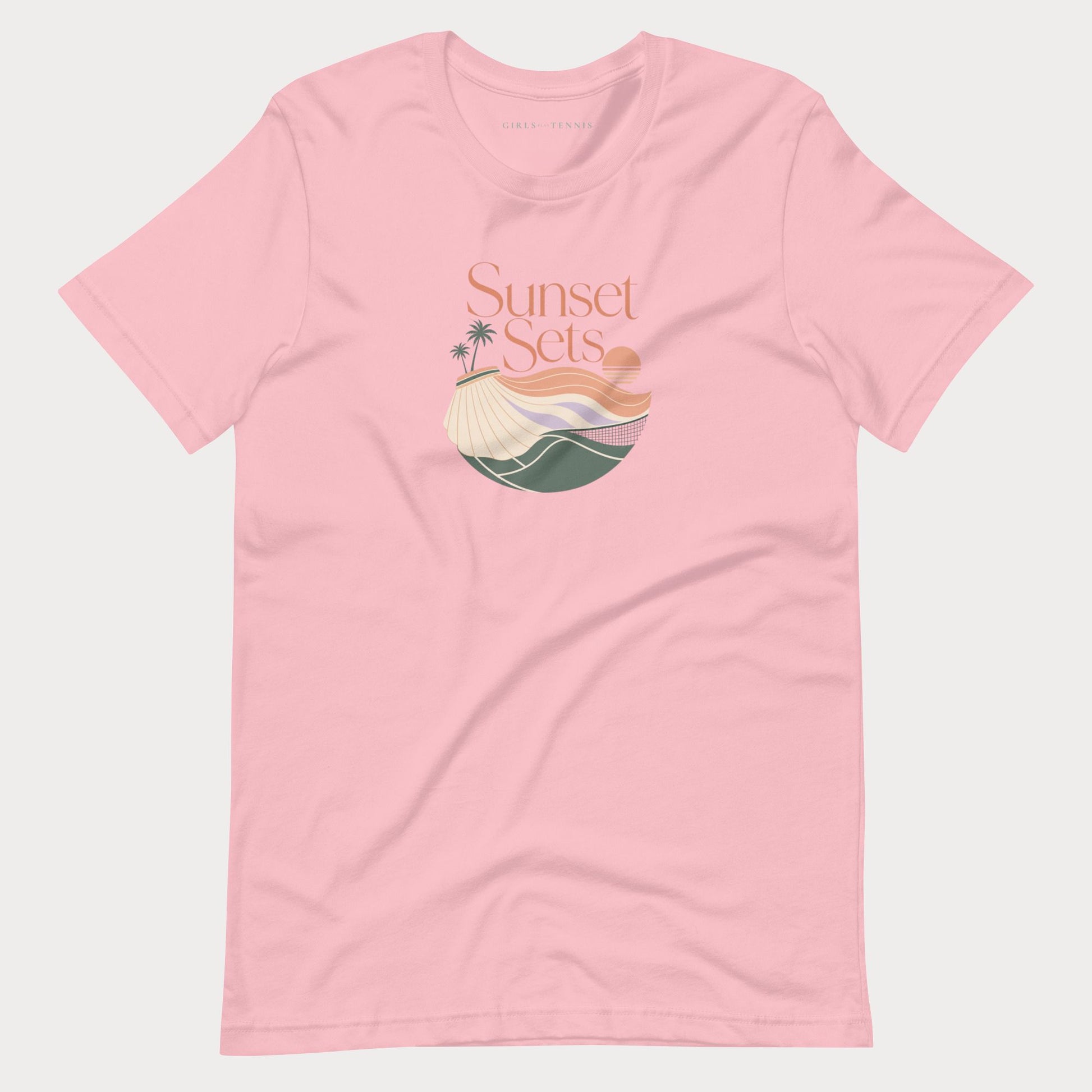 A light pink short-sleeve crewneck women's lifestyle tennis t-shirt featuring a retro-style graphic on the chest with the text 'Sunset Sets' above a stylized beach scene with palm trees, a sun, and waves.