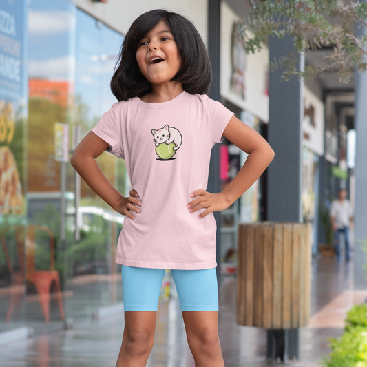 Young girl wearing a pink t-shirt with a cat graphic and blue shorts standing on a sidewalk.