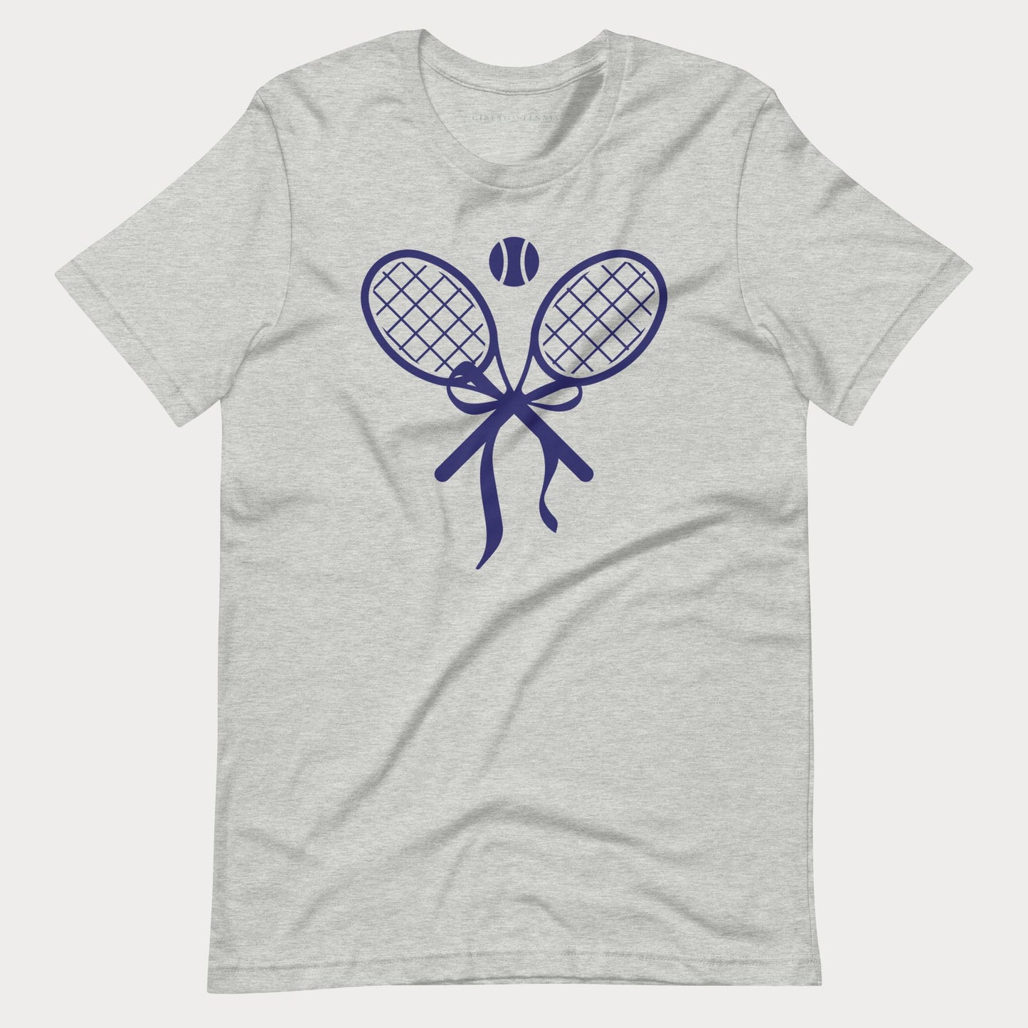 A light heather gray short-sleeve tennis t-shirt with a navy blue graphic of two crossed tennis rackets, a tennis ball, and a ribbon bow on the chest, displayed against a light gray background.