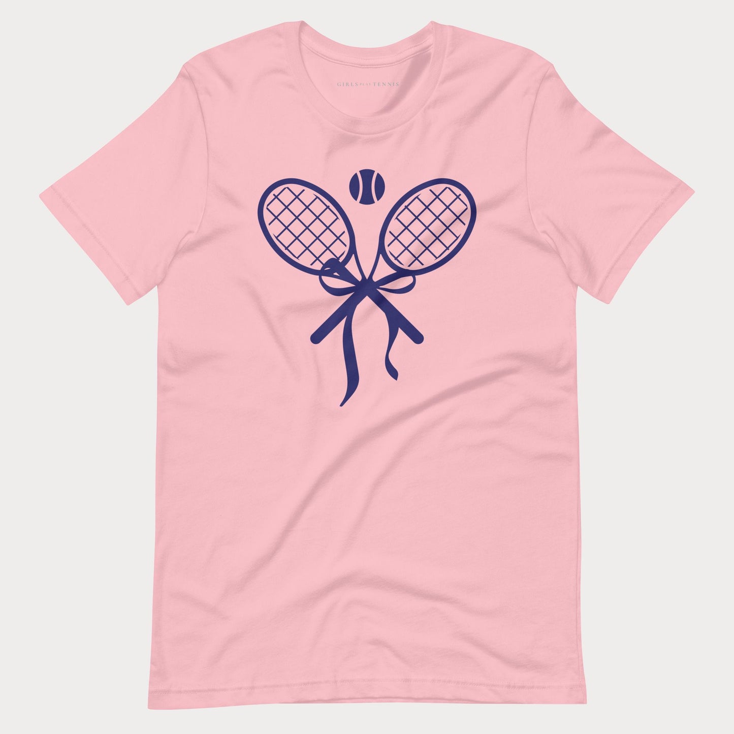 A light pink short-sleeve crewneck women's tennis t-shirt featuring a navy blue graphic of two crossed tennis rackets tied with a bow, with a tennis ball above them, shown on a light gray background.