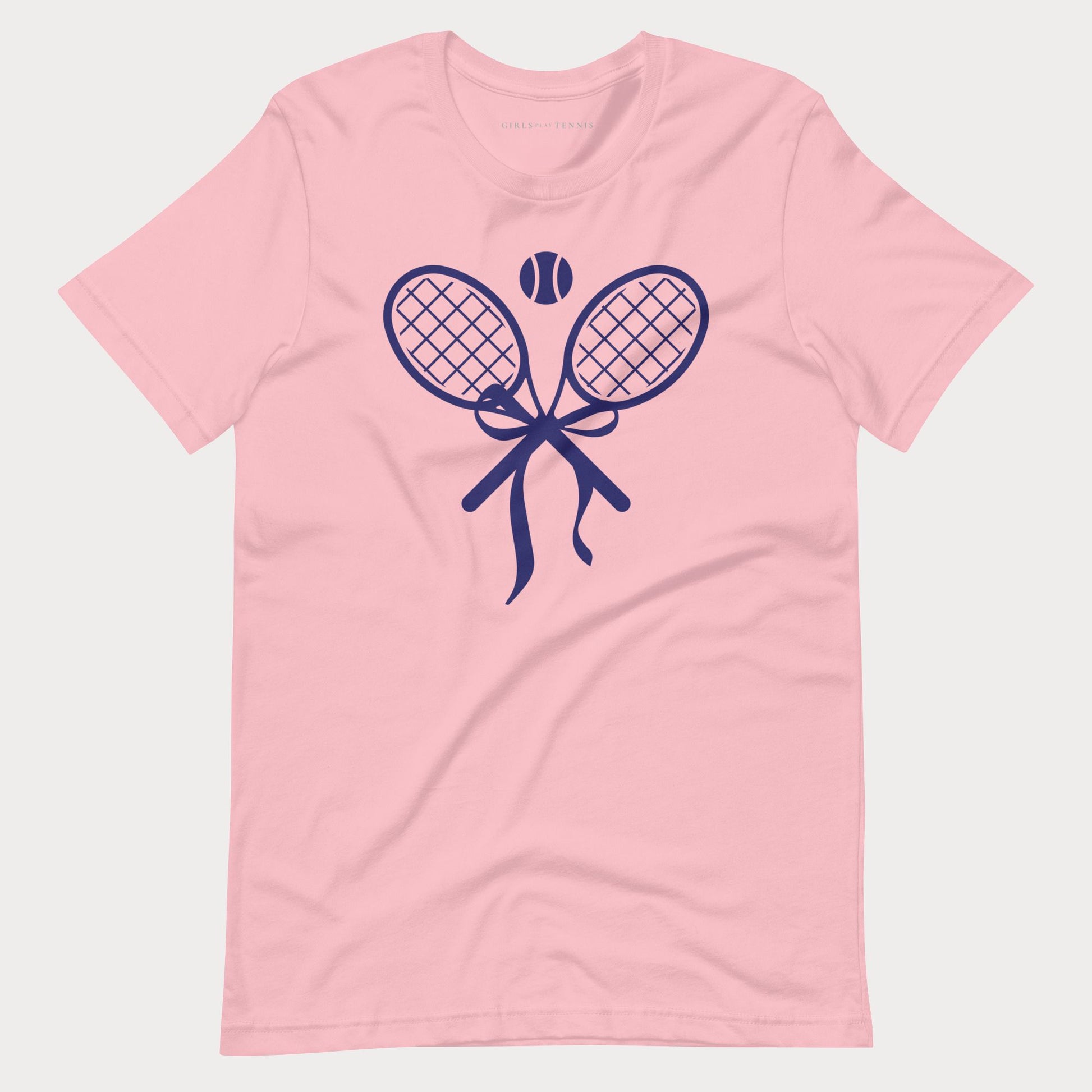 A light pink short-sleeve crewneck women's tennis t-shirt featuring a navy blue graphic of two crossed tennis rackets tied with a bow, with a tennis ball above them, shown on a light gray background.