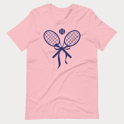 A light pink short-sleeve crewneck women's tennis t-shirt featuring a navy blue graphic of two crossed tennis rackets tied with a bow, with a tennis ball above them, shown on a light gray background.